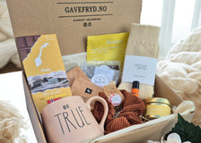 Gaveeske fra Gavefryd.no fylt med kuraterte produkter som en 'Be True'-kopp, norsk melkesjokolade fra tastes of norway, ullsokker fra Arthur & Betsy, leppepomade, scrunchie og hudpleie